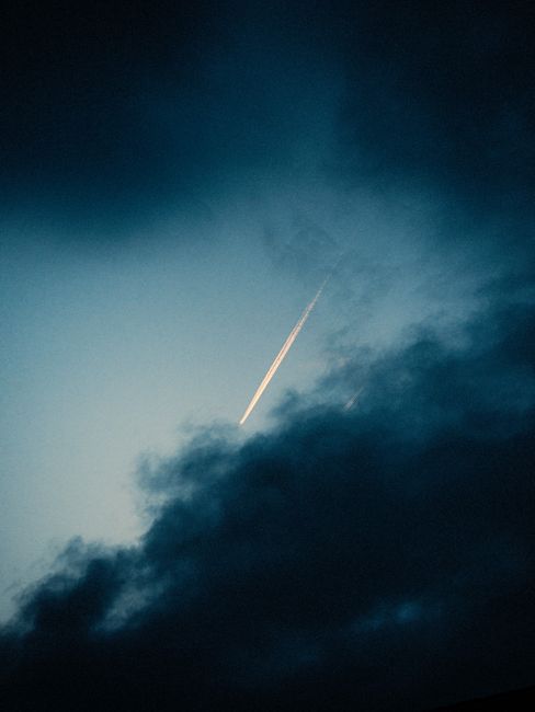 A dramatic twilight sky with a bright contrail illuminating through dark clouds.