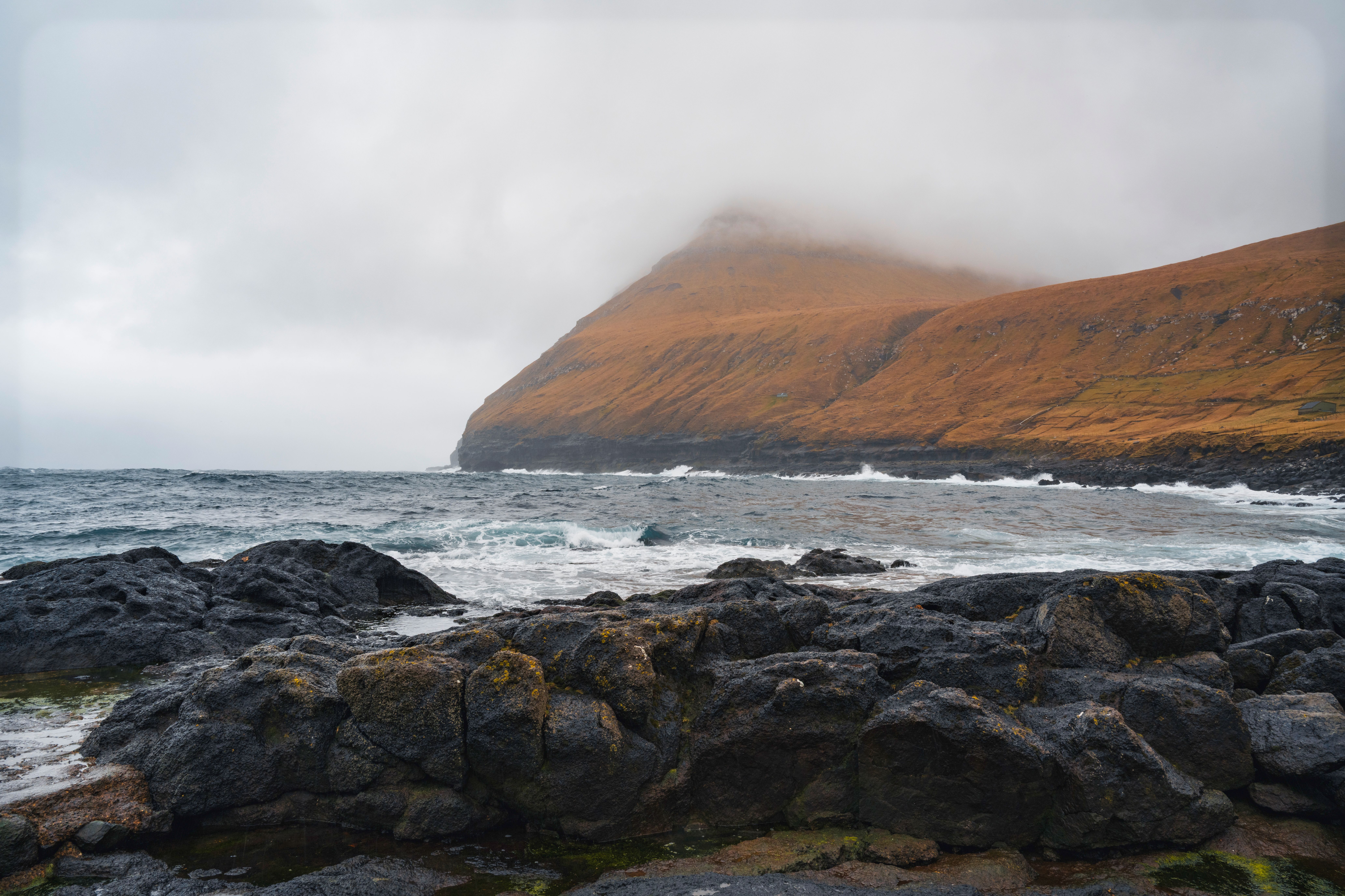 Moody coastal landscape in the Faroe Islands with rocky shore and misty hills.