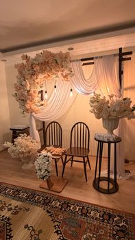Beautiful indoor wedding ceremony setup with floral arch and chairs, featuring warm lighting.