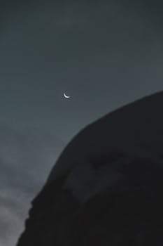 夜晚，一轮新月宁静地映照着山峰的黑色轮廓