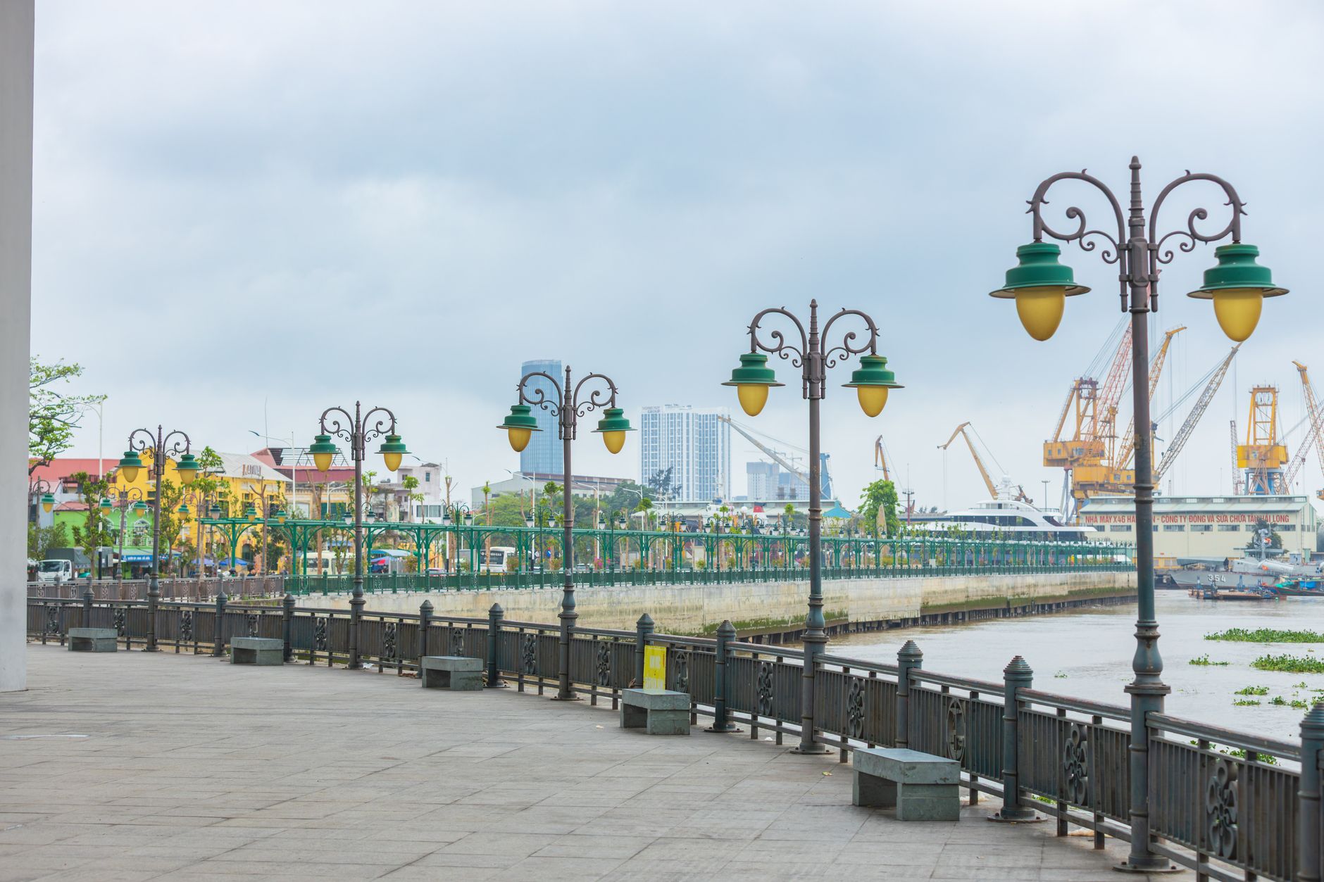 A scenic view of an urban riverside walkway with distinctive green lamp posts and cityscape background.