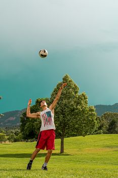 A young man jumps to hit a soccer ball in a sunny park setting.