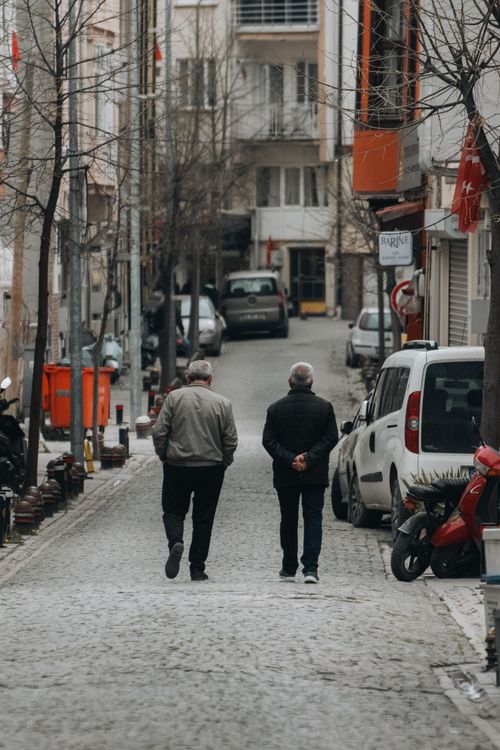 Free Two senior men walking on a narrow city street lined with parked cars and apartments, showcasing urban life. Stock Photo