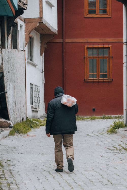 Free A man carrying a bag walks through a picturesque European alley with colorful architecture. Stock Photo