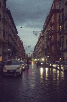 Atmospheric urban street scene at dusk, with cars lining a historic city street under a cloudy sky.