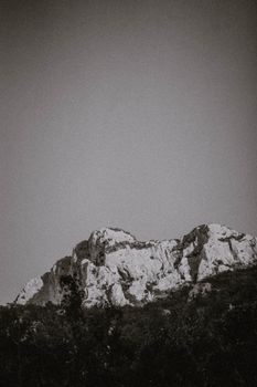 A dramatic black and white photograph of rugged mountain terrain under a clear sky.