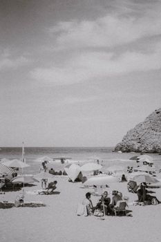 Timeless beach scene with people relaxing under umbrellas, captured in black and white.