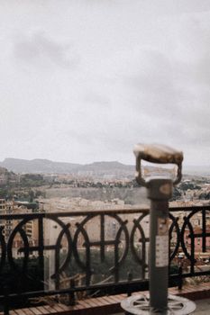 Urban landscape view featuring city skyline through tourist binoculars on a cloudy day.