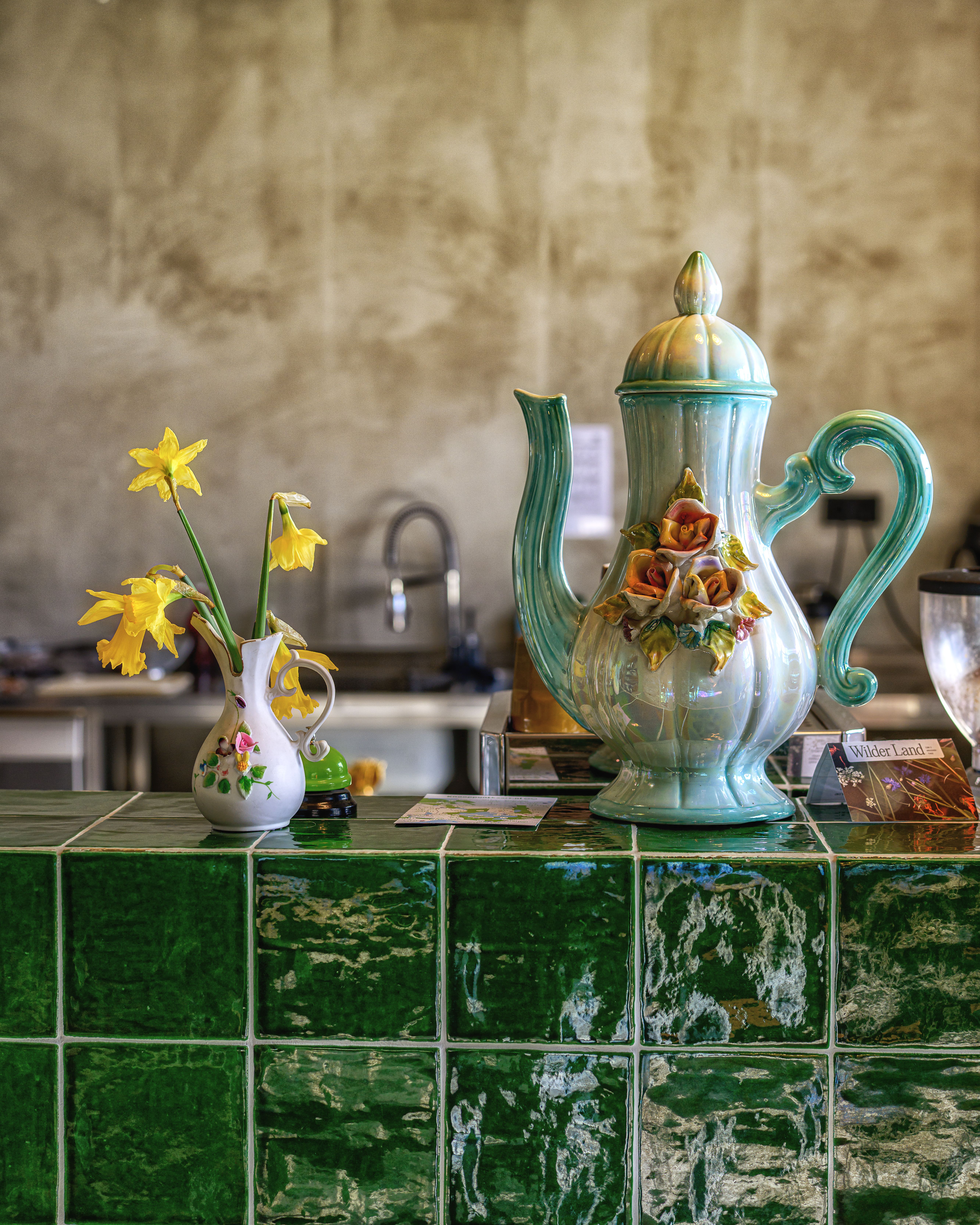Vintage ceramic teapot and daffodils on a green tiled counter, highlighting classic kitchen decor.