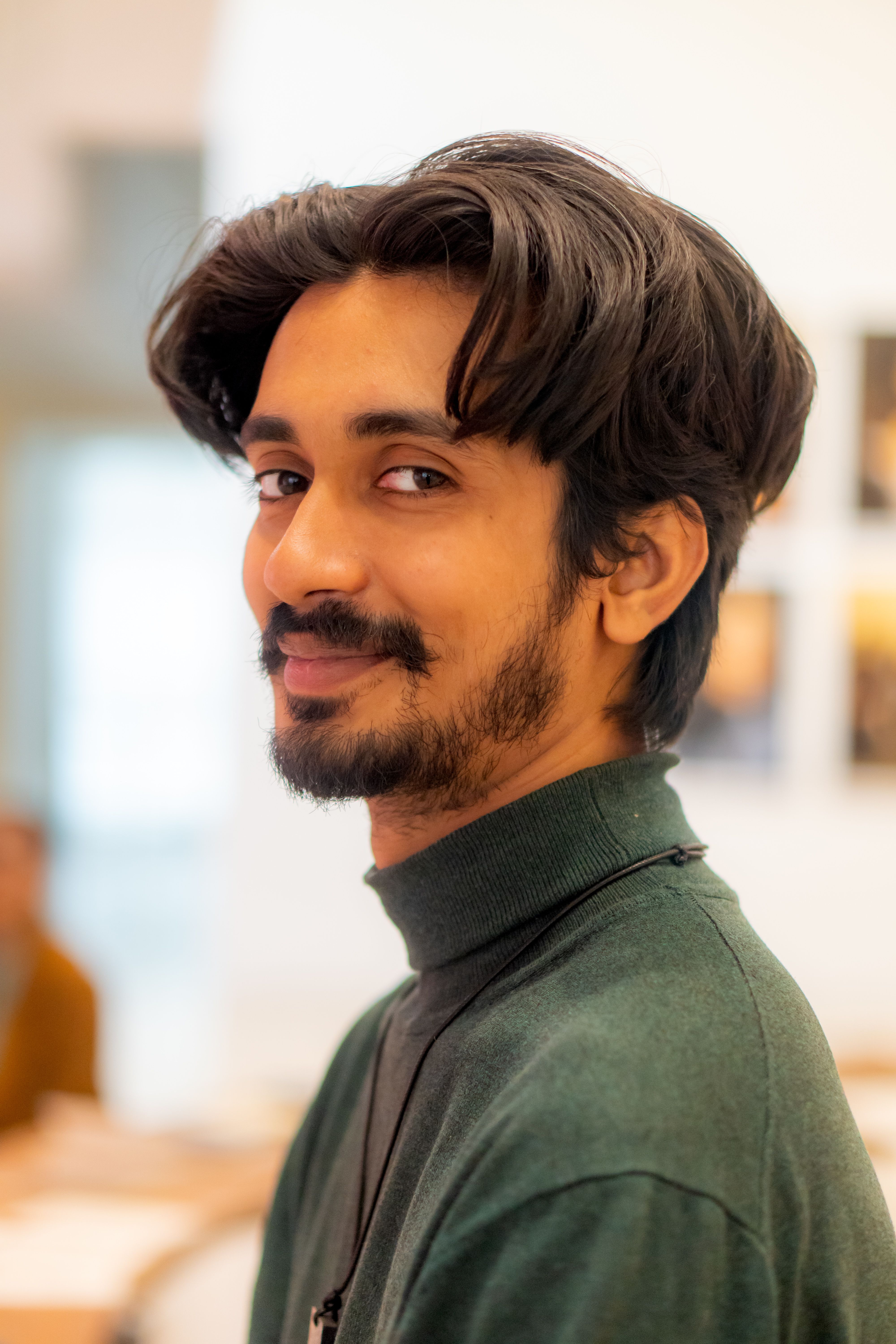 Casual portrait of a smiling young man in a relaxed indoor setting with soft focus background.