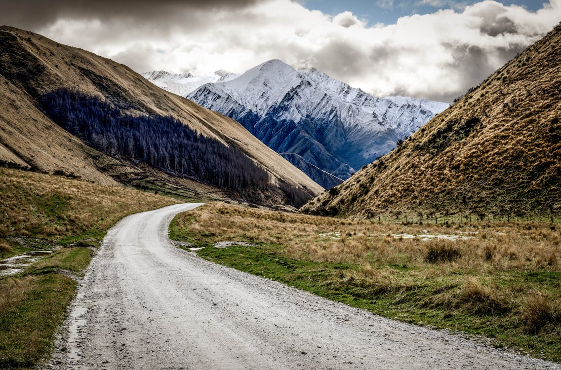 Gray Asphalt Road Near Brown and Green Mountains Under White Cloudy Sky