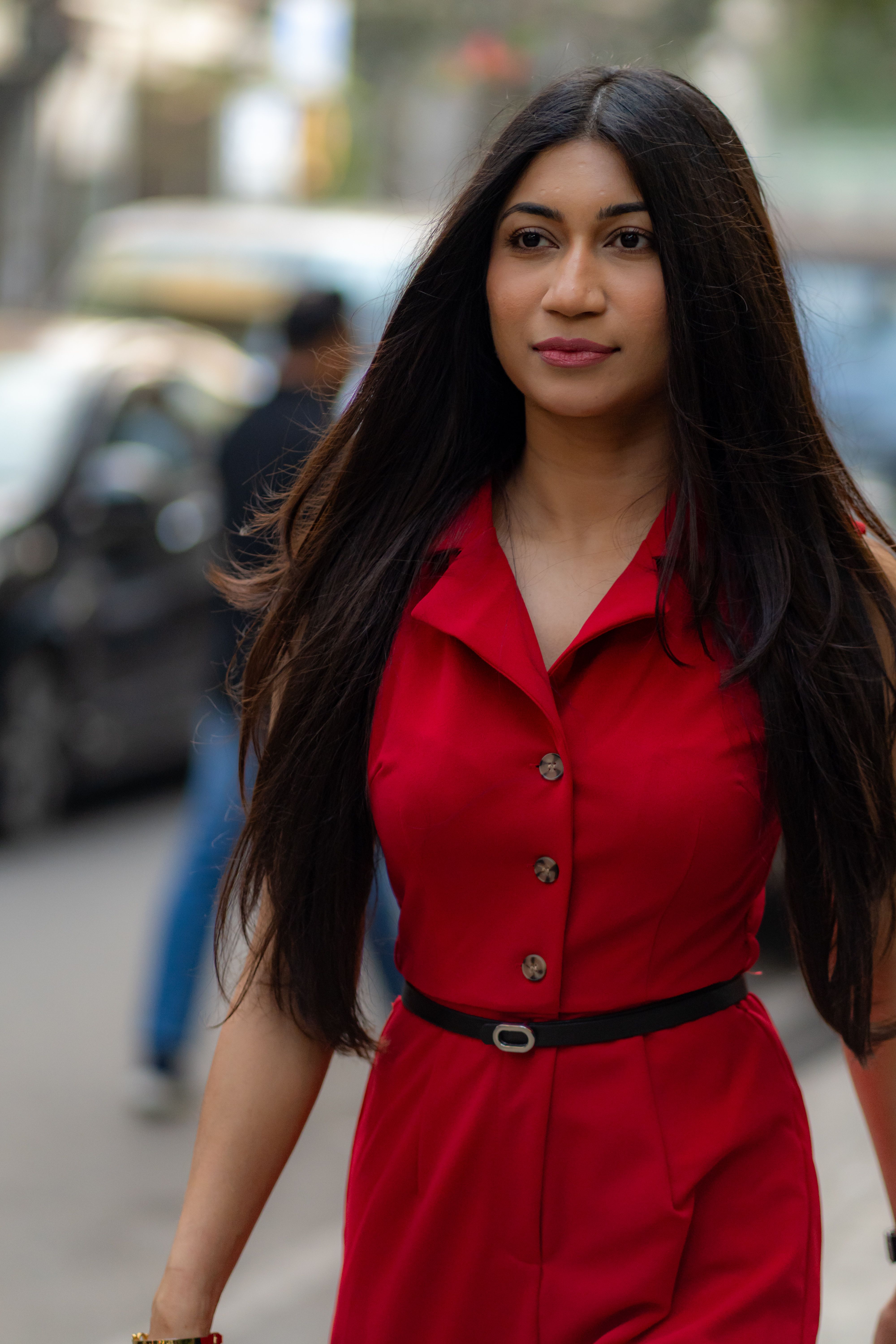 Elegant woman in a striking red dress confidently walking through a busy street in Dhaka, Bangladesh.