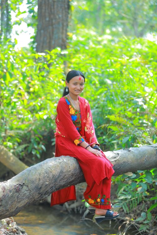 Free A woman in traditional attire sits boldly on a tree log in a lush, green forest. Stock Photo
