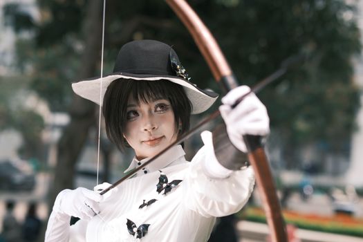 A stylish archer in Victorian attire draws a bow outdoors, showcasing focus and elegance.