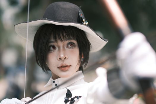 Close-up of a cosplay archer in focus, outdoors in Vietnam, showcasing artistic makeup and costume.