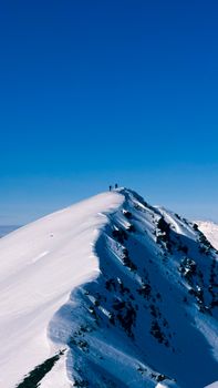 Dramatic view of an alpine mountain peak with hikers reaching the summit under a clear blue sky.
