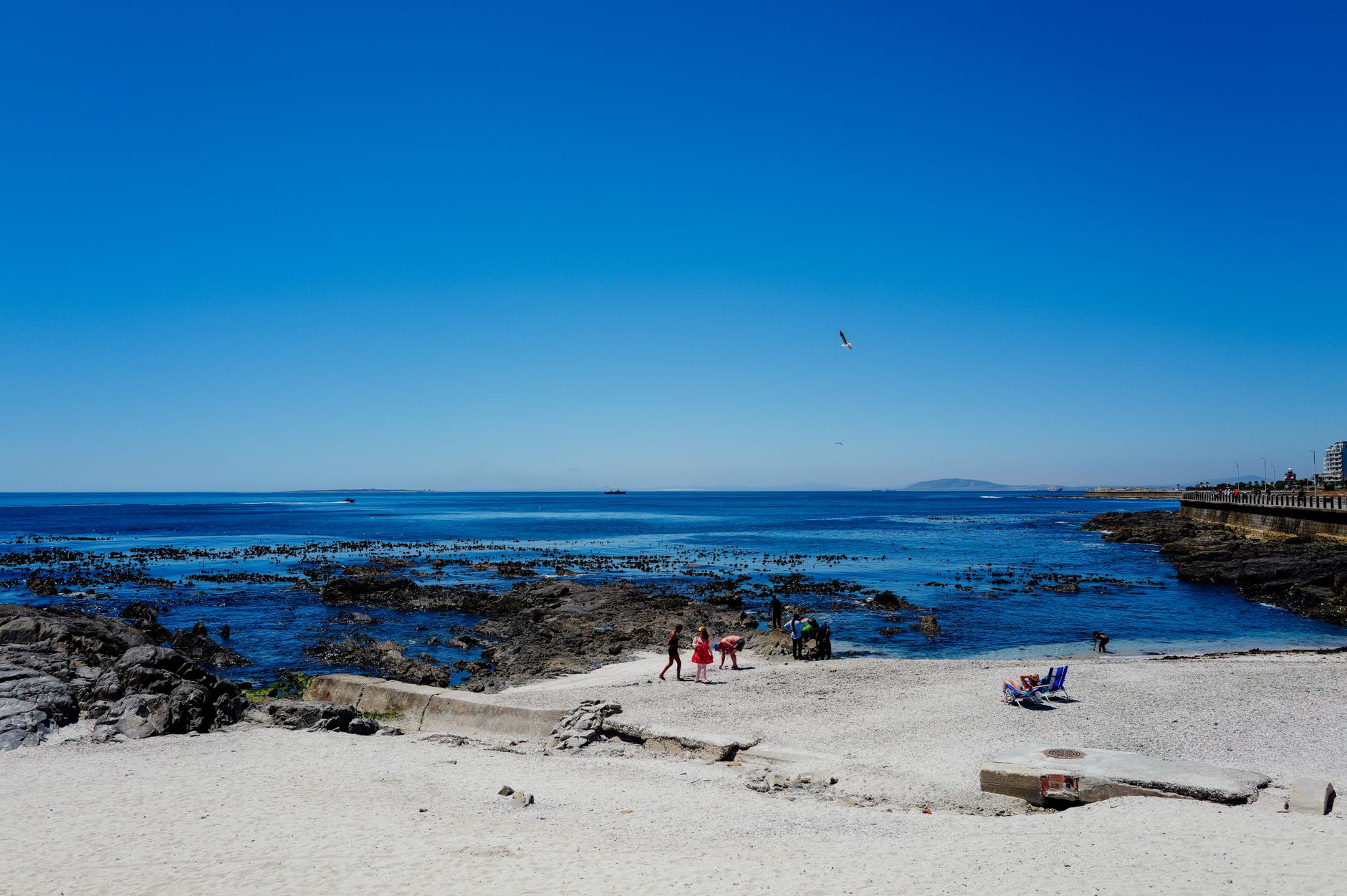 A vibrant summer scene at a rocky beach with people enjoying the sun and sea views.