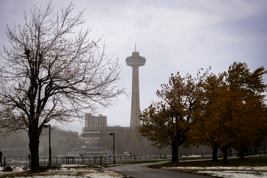 Skylon Tower rising through autumn mist at Niagara Falls, New York. A serene autumn scene with colorful trees.