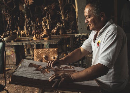在木制雕塑上工作的白色polo衫的男人
