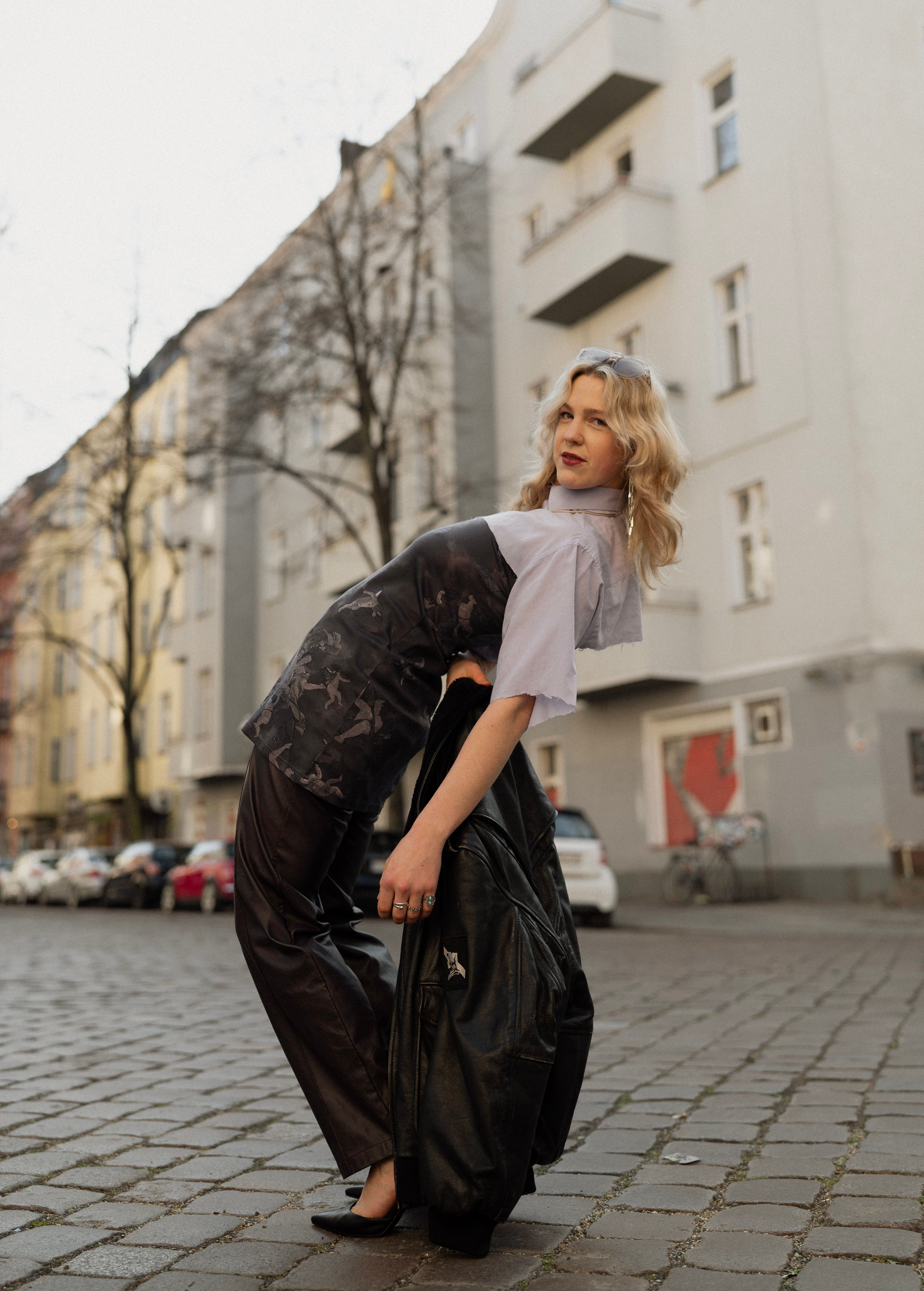 Stylish young woman striking a pose on a cobblestone street in Berlin with classic architecture behind her.