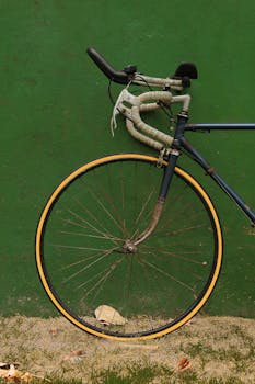 一辆老式赛车自行车的车轮特写镜头，靠在纹理丰富的绿色墙上