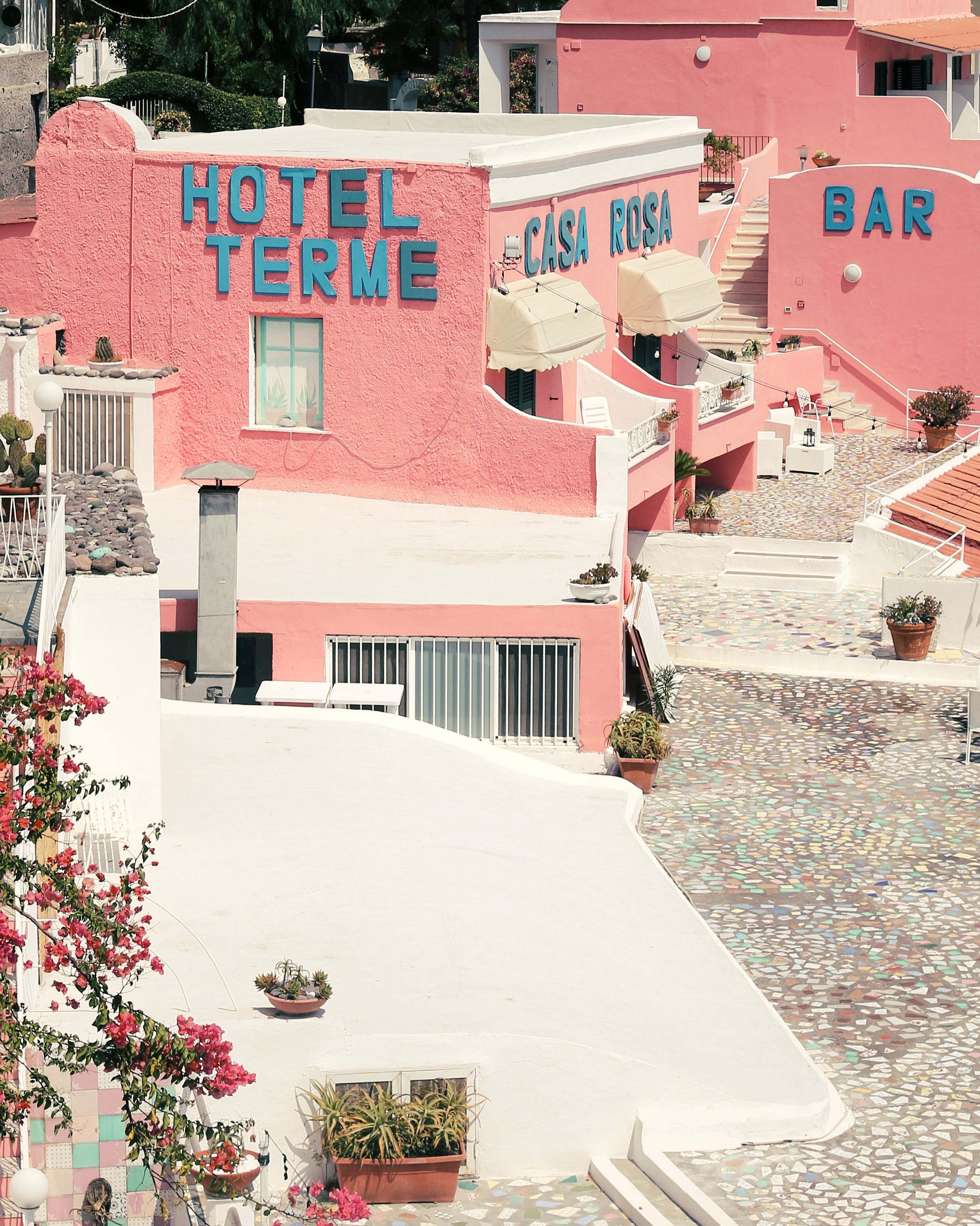Bright pastel pink hotel with vibrant signage in a sunny outdoor European setting, ideal for travel and architecture themes.