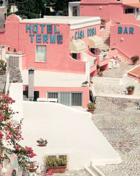 Bright pastel pink hotel with vibrant signage in a sunny outdoor European setting, ideal for travel and architecture themes.