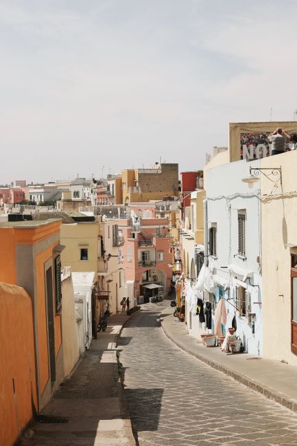 Colorful narrow street in a Mediterranean town with pastel buildings and people enjoying the day.