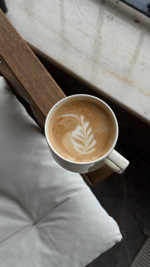 Free Top view of a coffee cup with intricate latte art on a wooden chair. Ideal for relaxation and coffee themes. Stock Photo