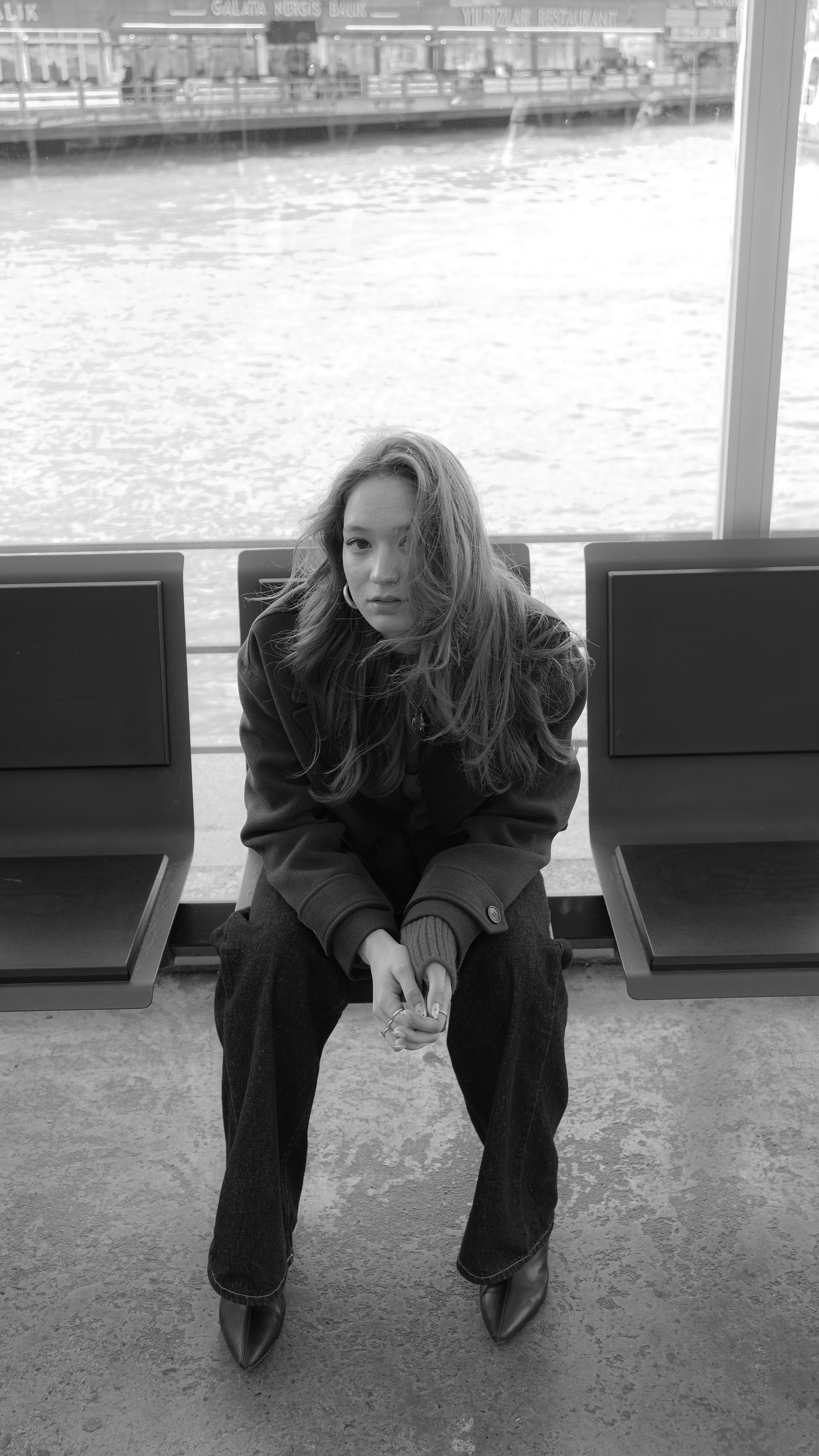 A young woman sits pensively on a bench by the water in black and white, İstanbul.