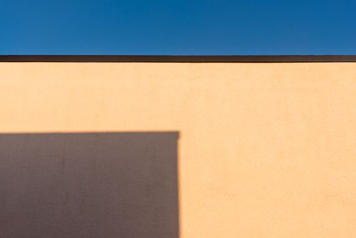 Free A minimalist photo of a wall with a sharp shadow against a clear blue sky. Stock Photo