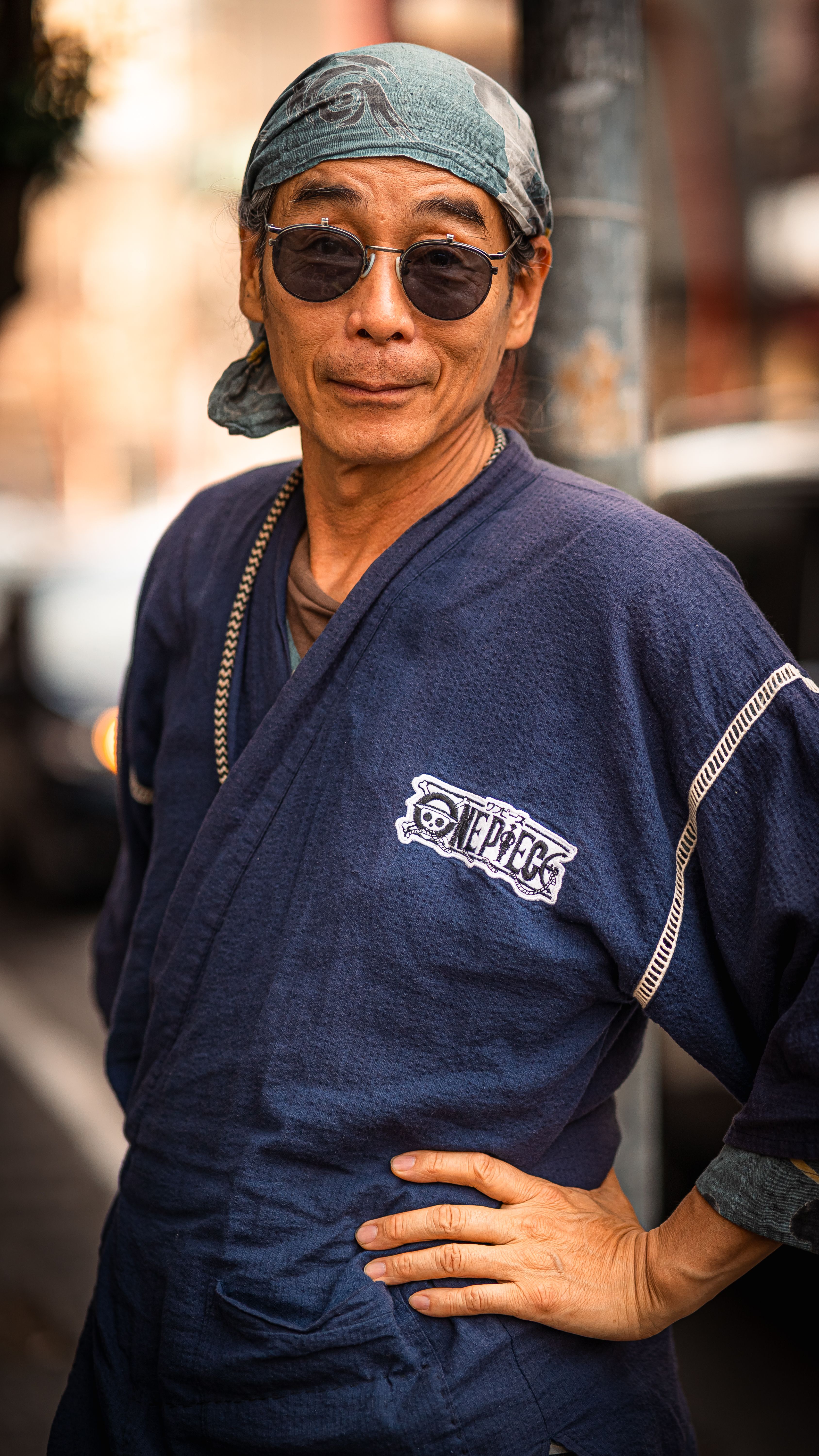 Stylish older man wearing sunglasses and headscarf looking confidently at the camera outdoors.