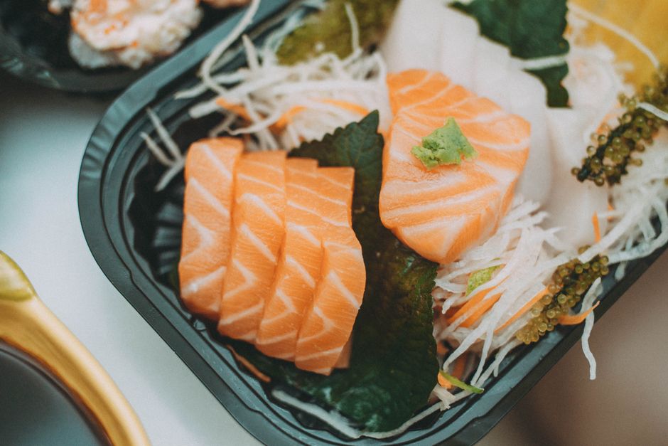 Close-up of fresh salmon sashimi served on a black plate with wasabi garnish.
