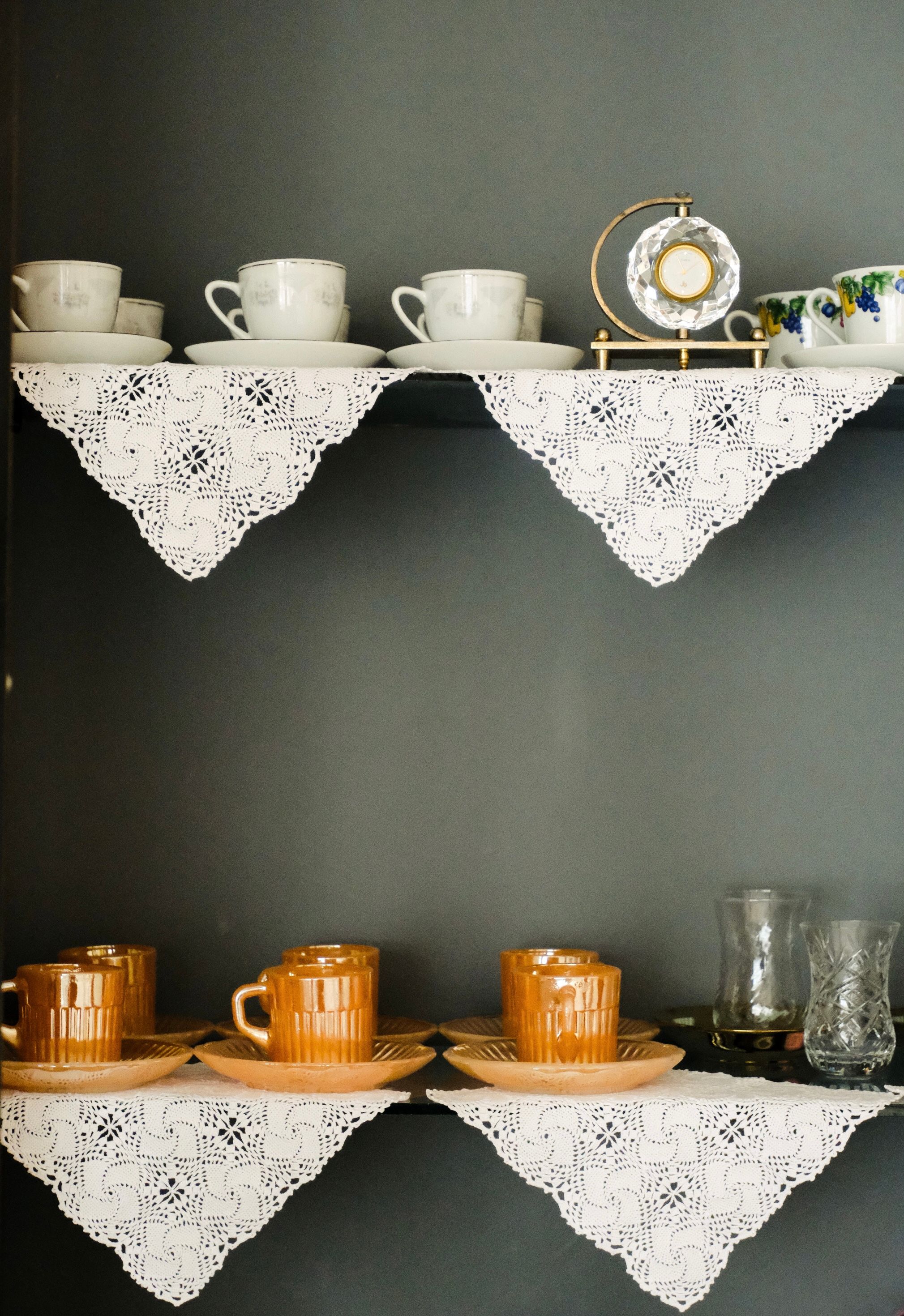 Vintage china teacups and amber glass mugs on shelves lined with crocheted doilies