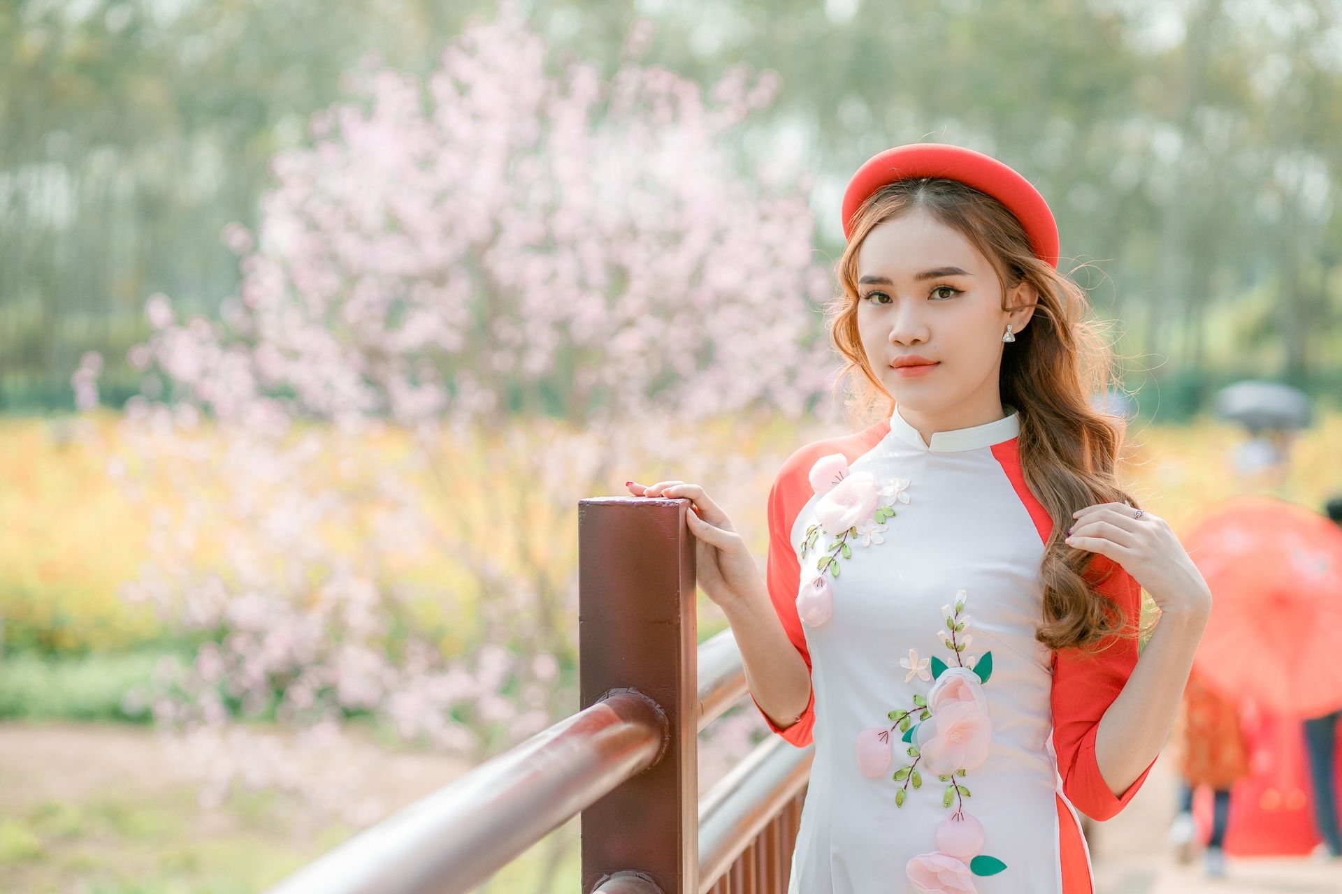 A young woman in traditional attire poses on a sunny day with cherry blossoms in the background.