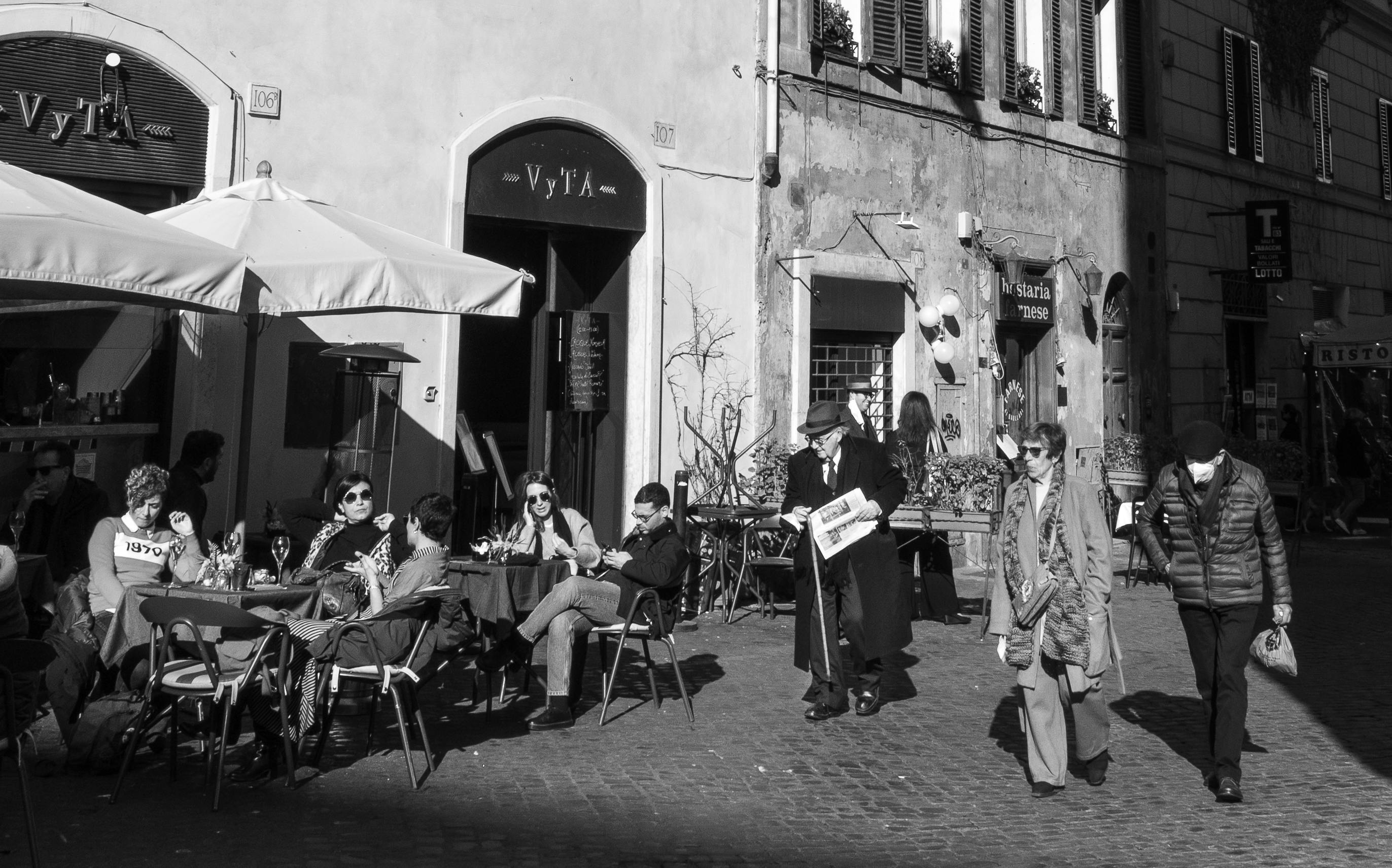Candid street scene in Rome, capturing city life with people dining outdoors in black and white.