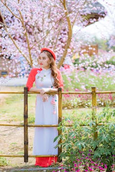 一位身着传统服装的优雅女子，静静立于栅栏旁，身旁樱花盛开，散发着宁静的气息