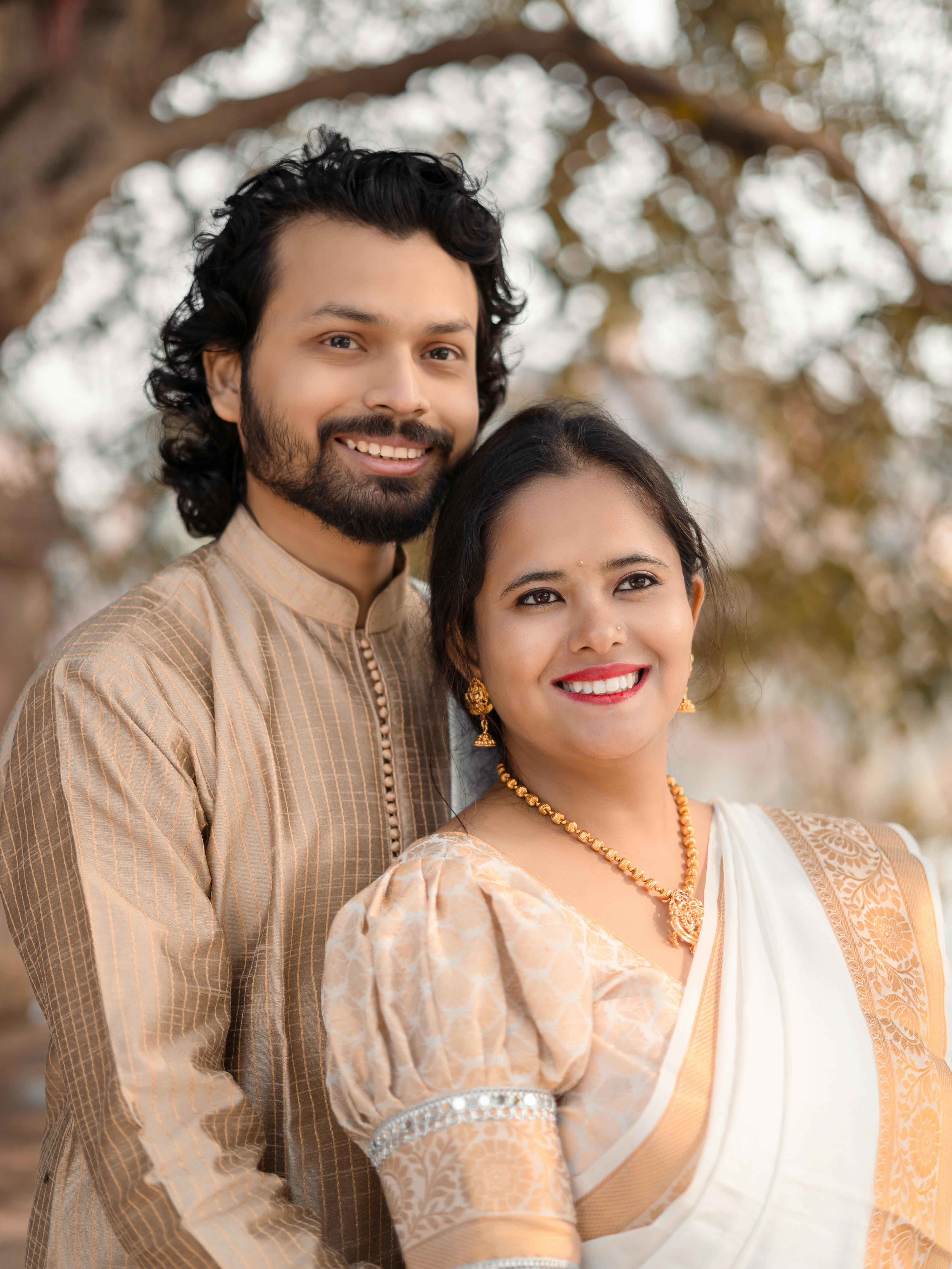 A joyful Indian couple in traditional attire posing outdoors, reflecting love and elegance.