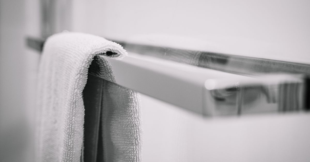 Uma toalha branca e limpa está pendurada em um suporte de toalhas cromado brilhante, criando uma estética minimalista e moderna para o banheiro.