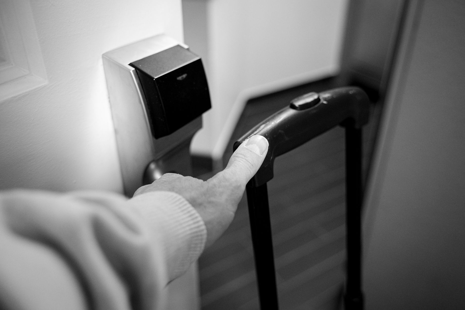 A monochrome photograph of a hand opening a hotel room door with a luggage handle.