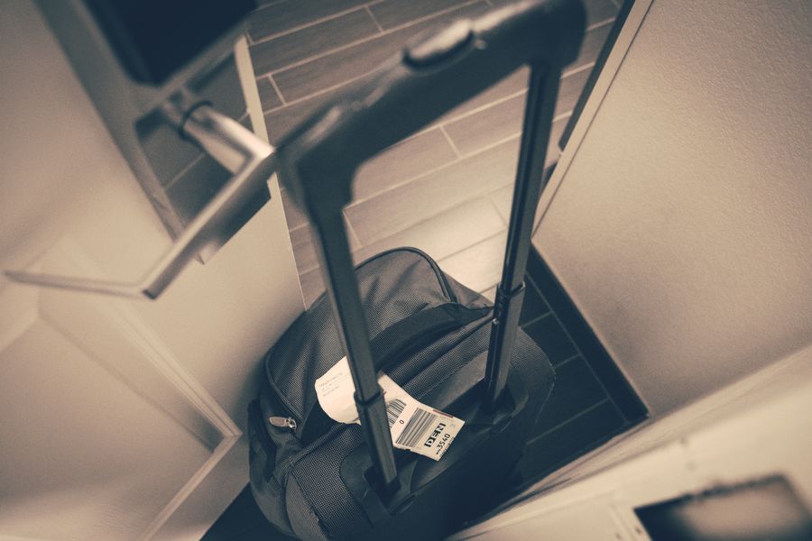 Travel suitcase with tag by hotel door, symbolizing travel or business trip.