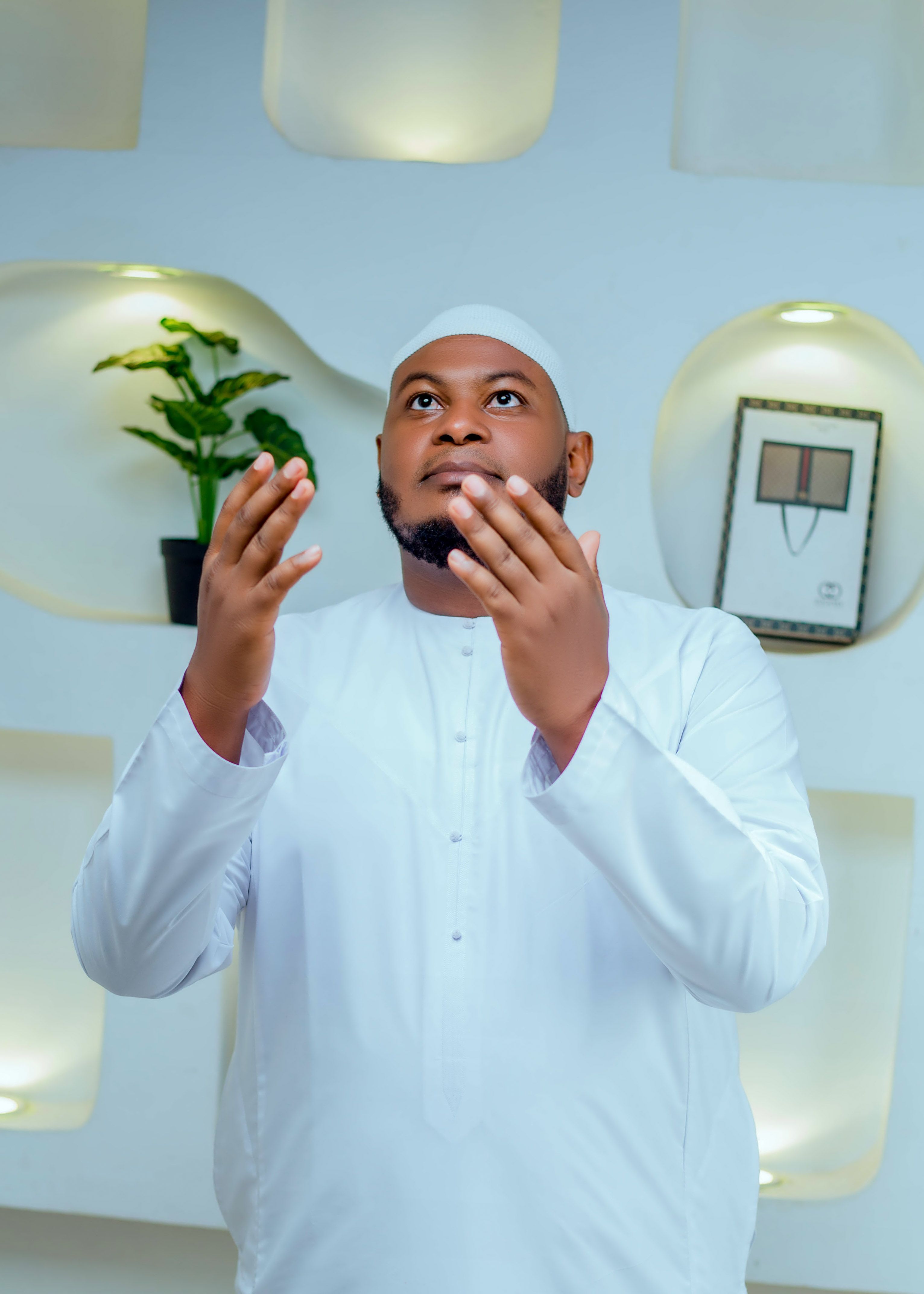 A man in white traditional attire praying indoors, exuding spirituality and devotion.
