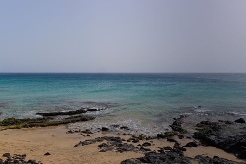 Free Breathtaking view of the ocean meeting a rocky shore under a clear blue sky. Stock Photo