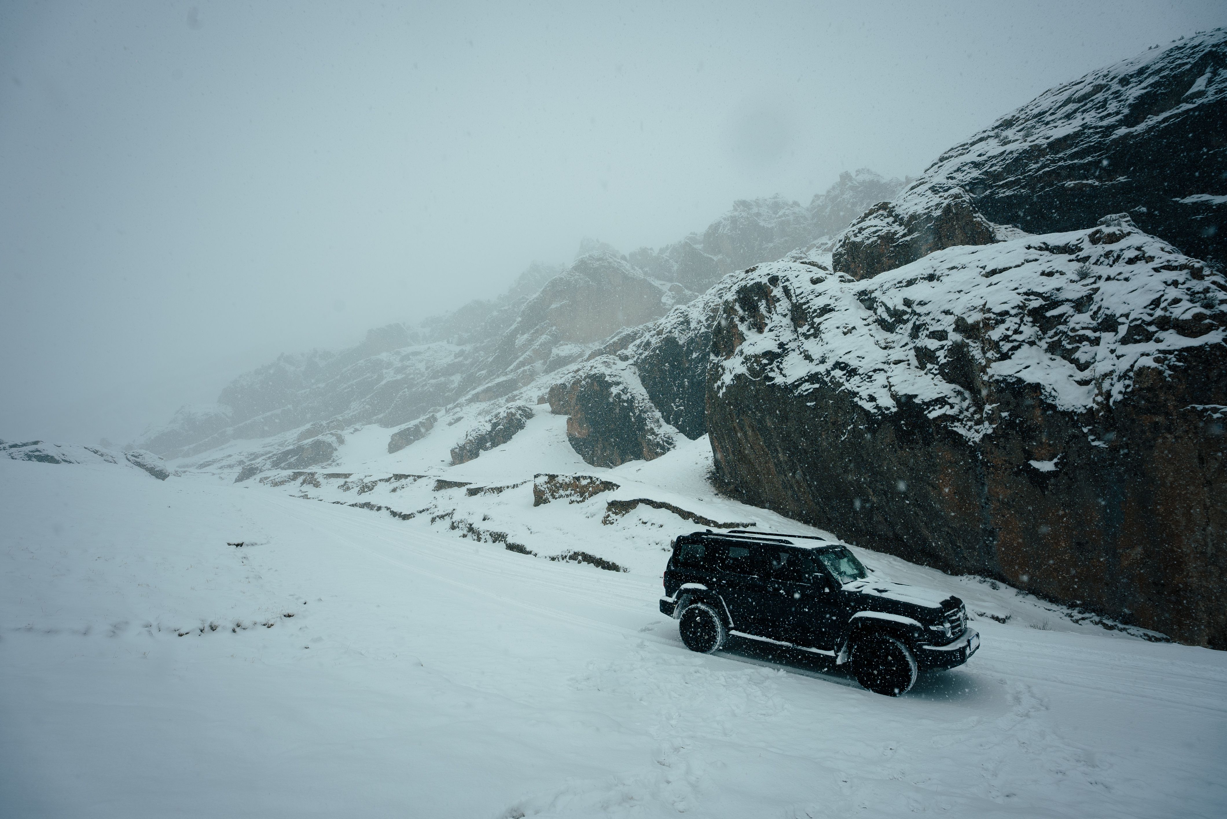 A 4x4 vehicle navigates snowy mountain terrain during a winter storm.