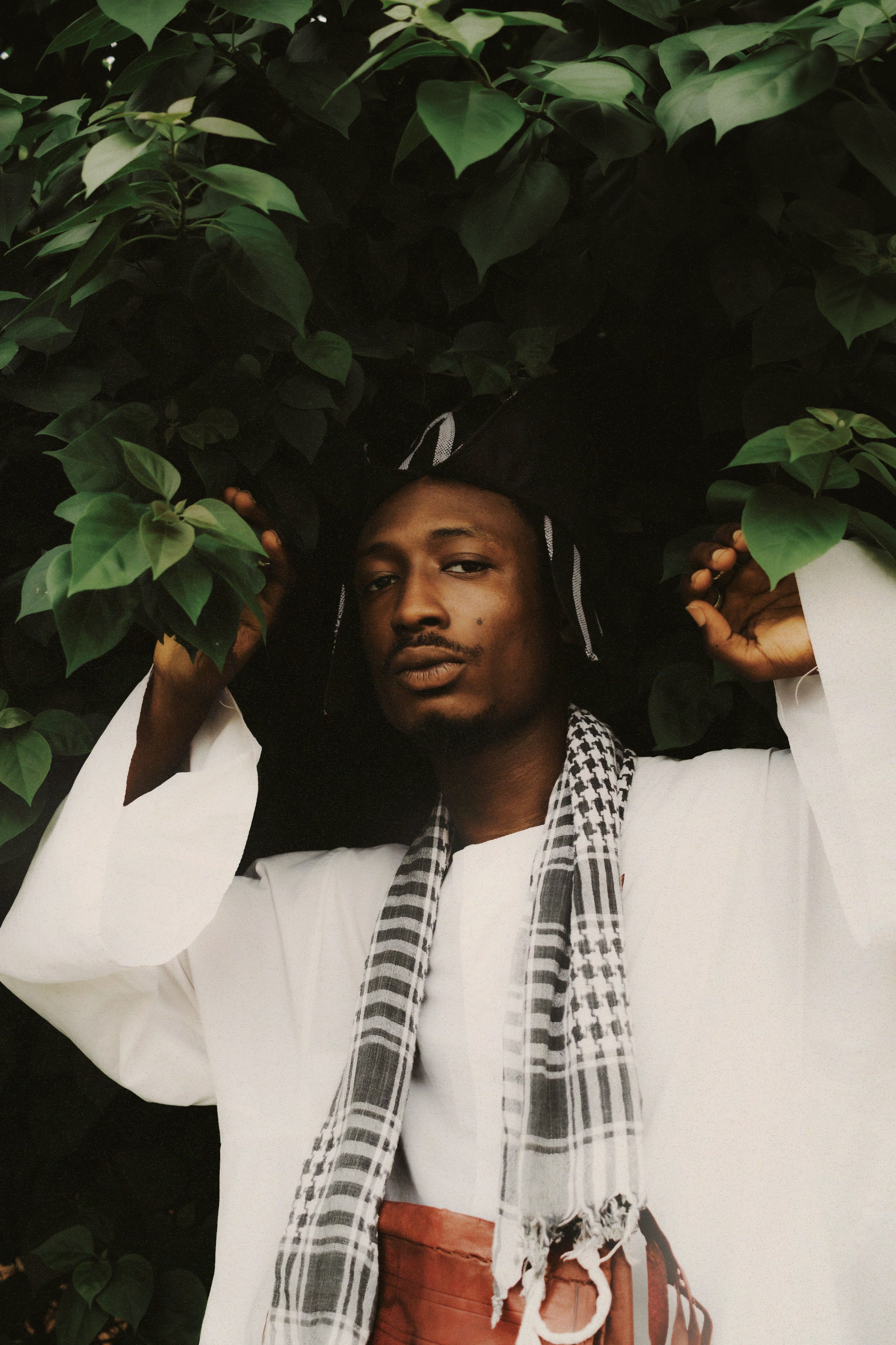 Man in traditional Nigerian attire with greenery background, depicting cultural heritage.