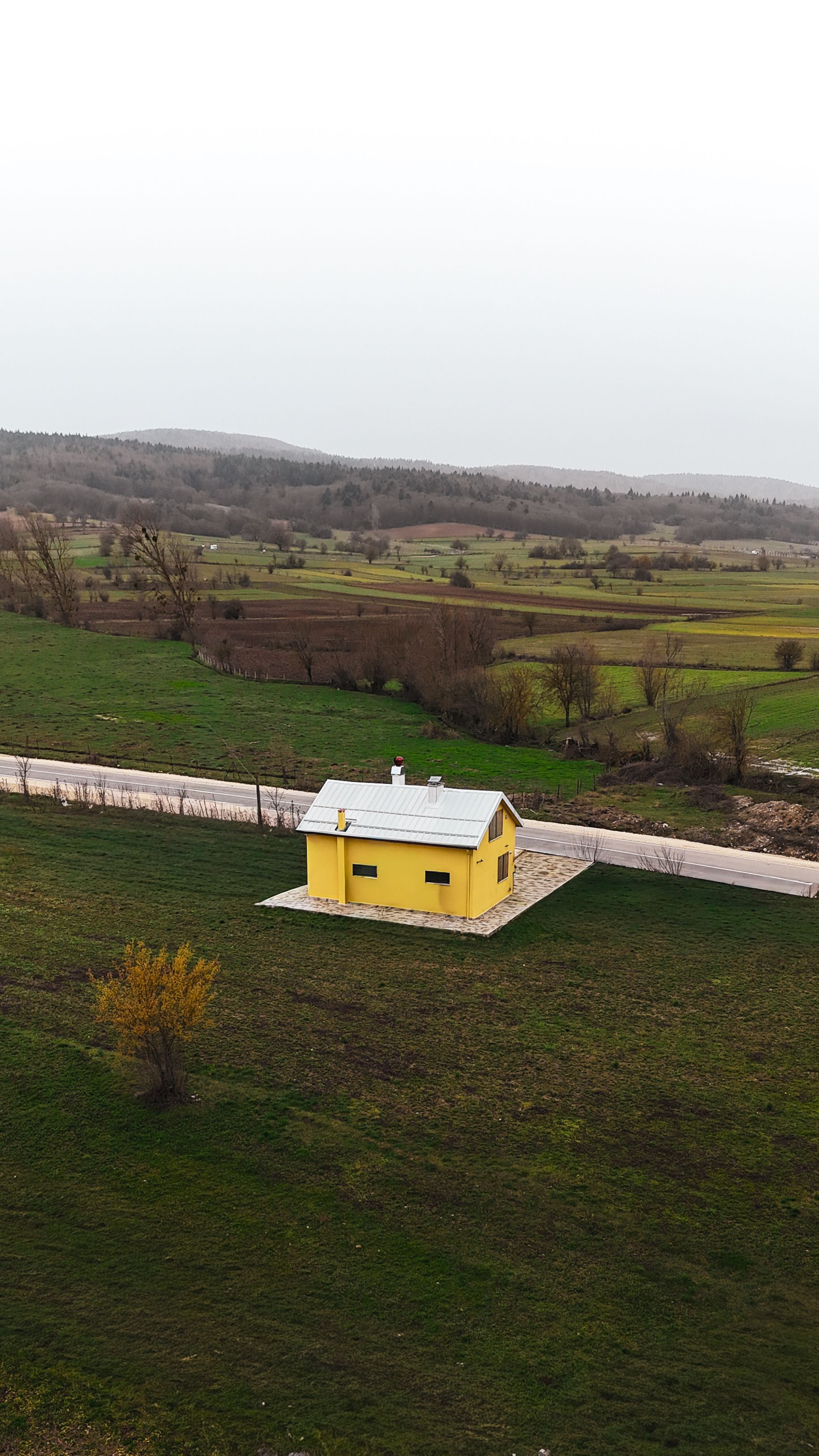 Aerial view of a bright yellow house in the lush green countryside of Bolu, Türkiye, offering a serene rural landscape.