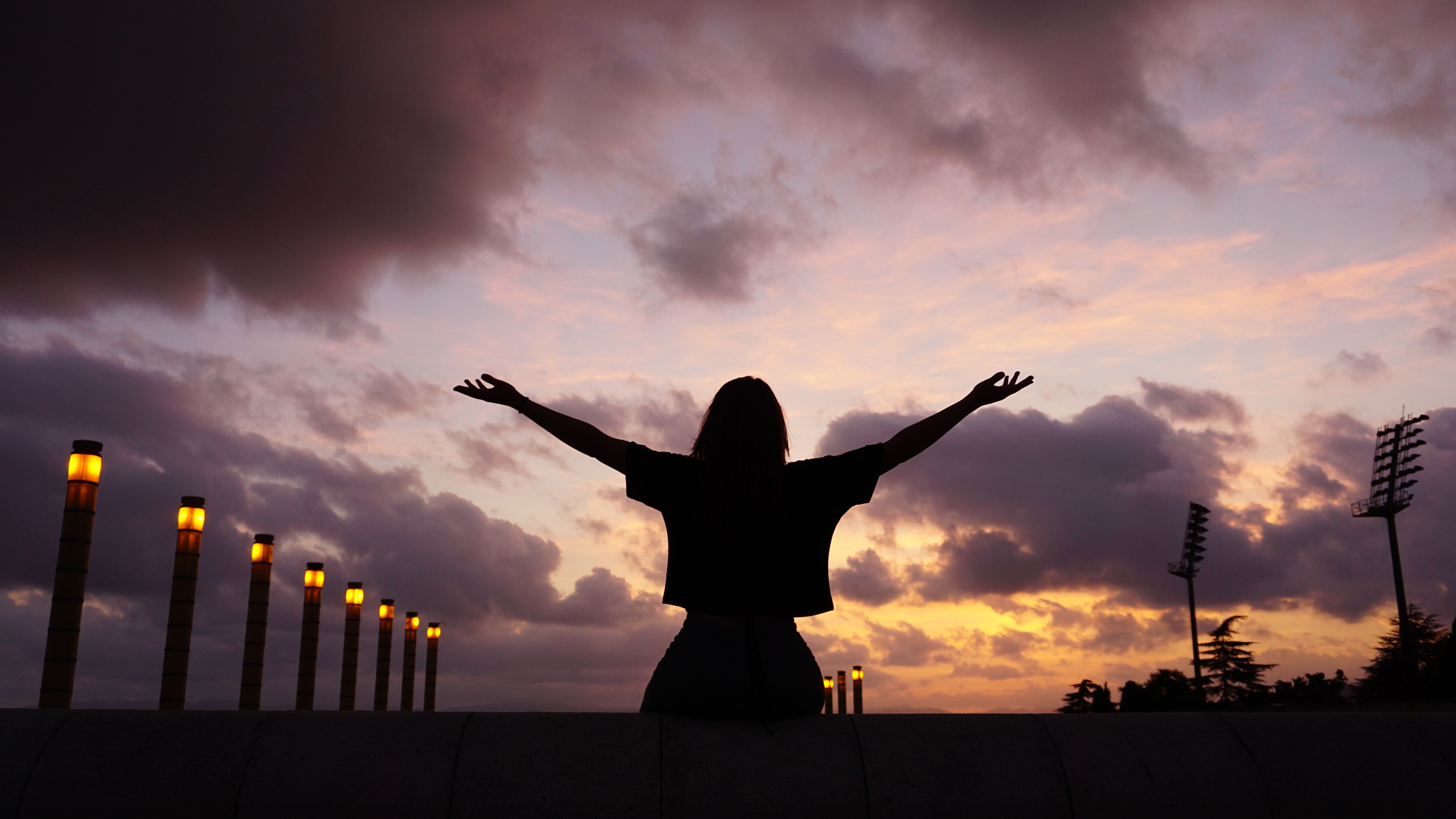 Silhouette of a person with arms outstretched against a dramatic sunset sky, symbolizing freedom and nature.