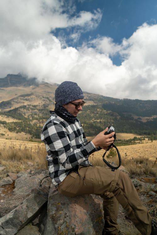 Free A person examines photos on a camera while sitting on a rock in scenic mountains. Stock Photo