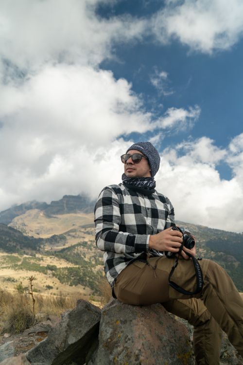 Free A young man with a camera enjoys the mountain landscape, capturing nature's beauty. Stock Photo