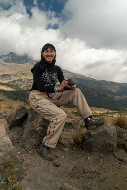 Free Female photographer posing with camera on a rocky mountain terrain under a cloudy sky. Stock Photo